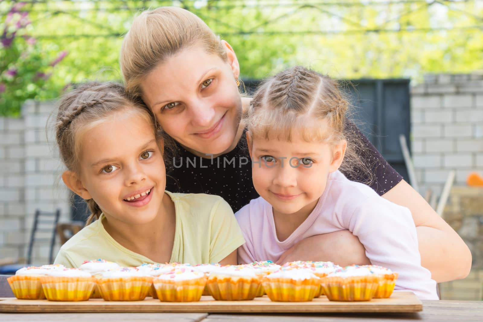 Mother hugging her daughters who cook delicious cupcakes