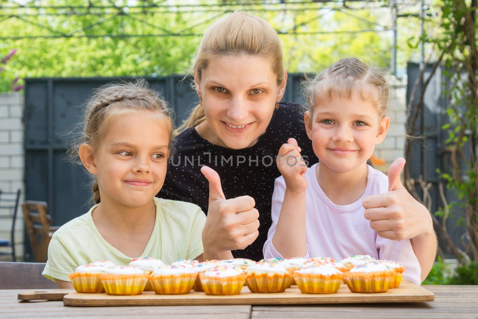 Mother and two daughters show a thumbs-up, and dress easter cupcakes