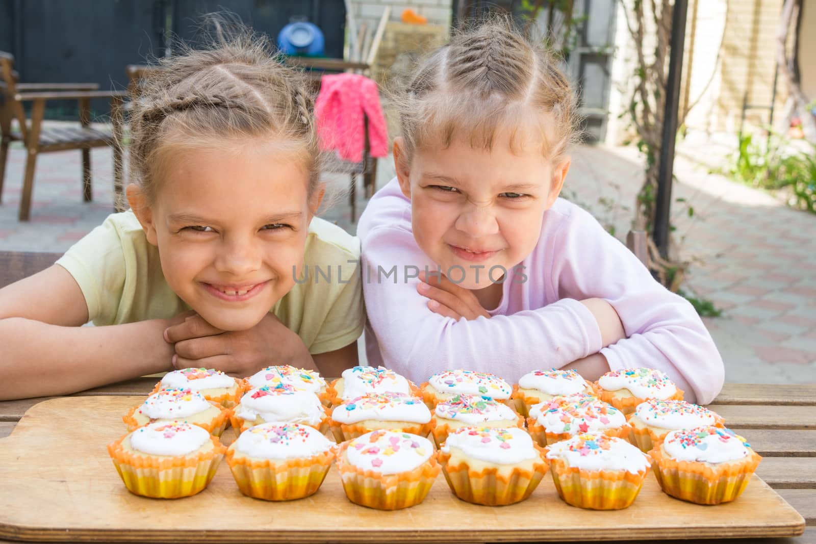 Two girls pretending funny faces, sitting in front of easter cupcakes