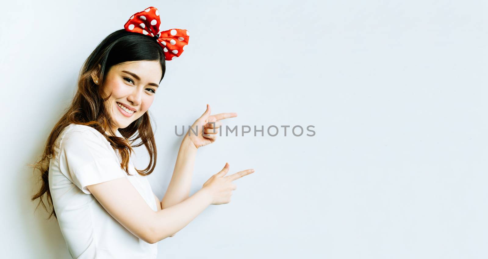 Beautiful asian university or college student woman wearing funny bow headband, pointing at copy space on whiteboard background by beer5020