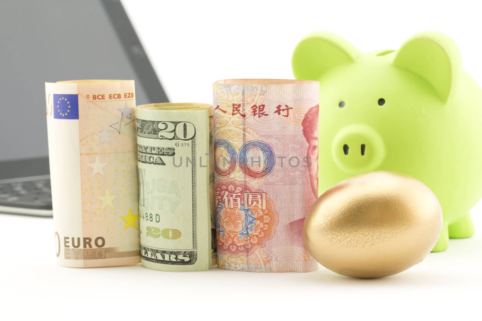Three currencies, euro, dollar, and yen, placed with gold nest egg with computer and bank in background reflect strategic global investment and success.