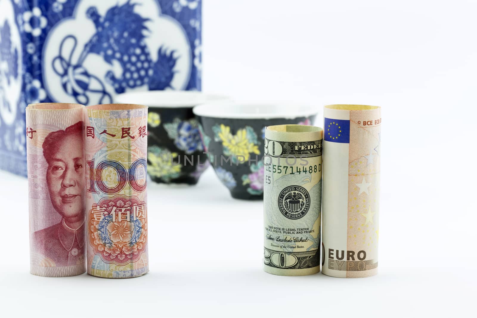 Chinese yuan currency, American money, and European Union euro stand in front of Asian porcelain tea cups and storage jar suggesting Asian meeting and business finance discussions. 