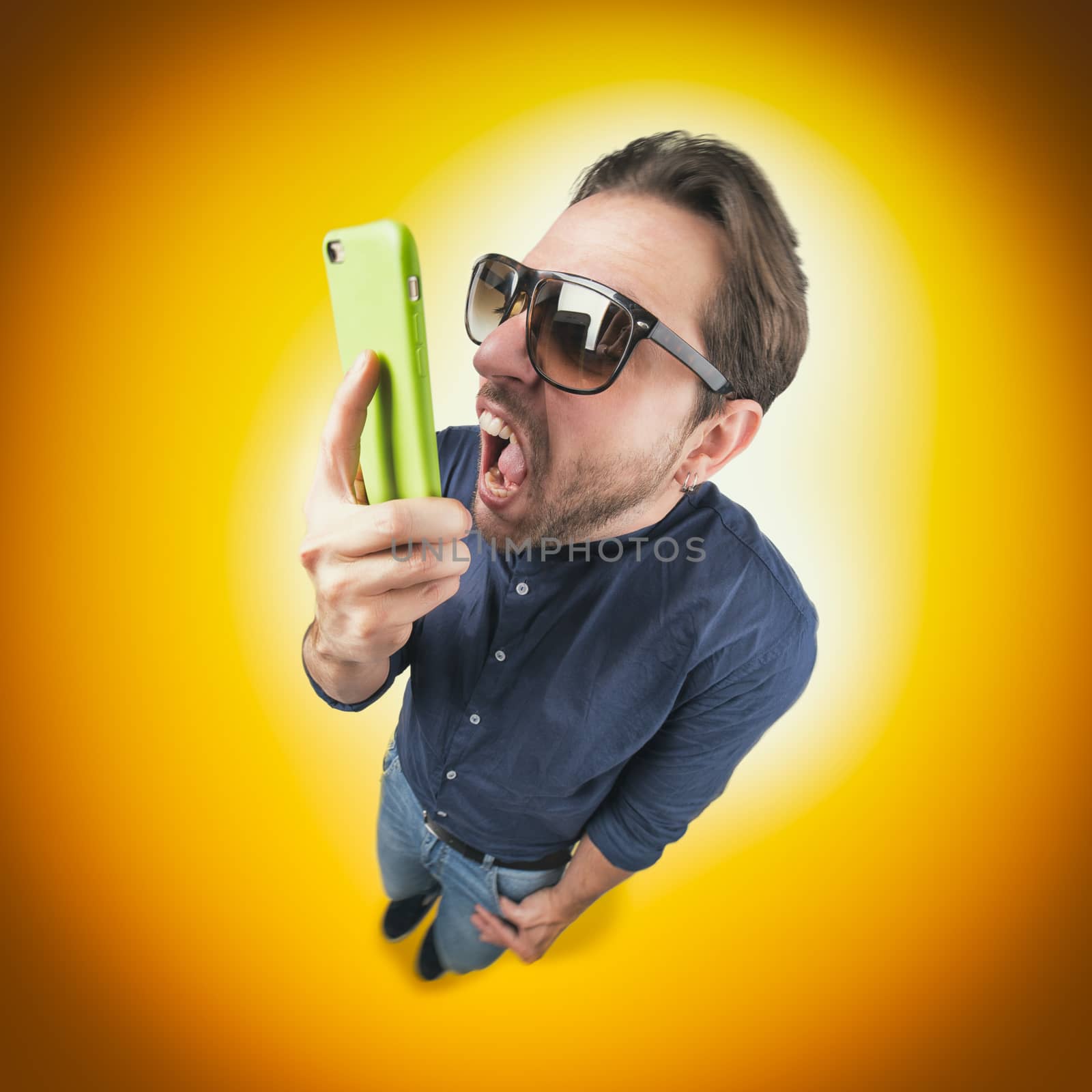 Funny young man screaming on his mobile phone wear a pair of sun glasses on color background