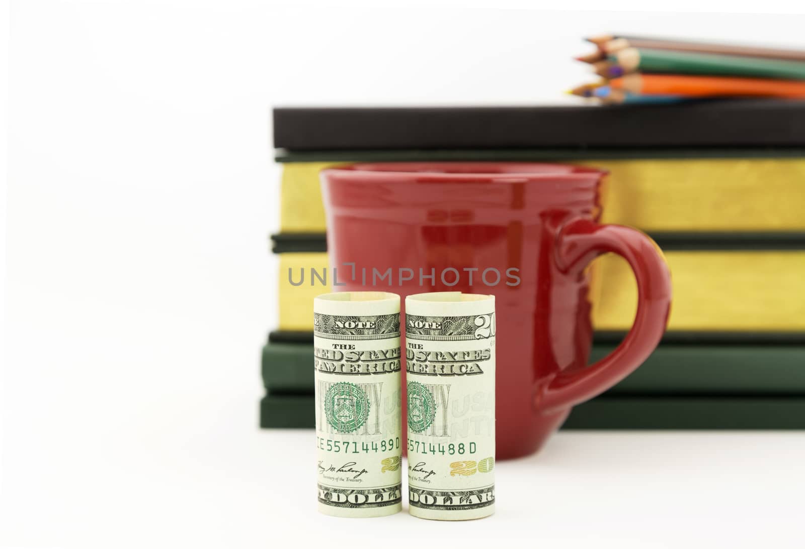 Careful accounting and investment work reflected in red mug, United States money, books, and pencils.  Selective focus on currency. White background with copy space.  