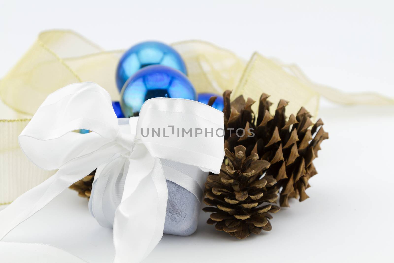 Gray velvet jewelry box wrapped in white.  Gift placed with pine cones, blue glass Christmas balls, and gold ribbon on white background.  