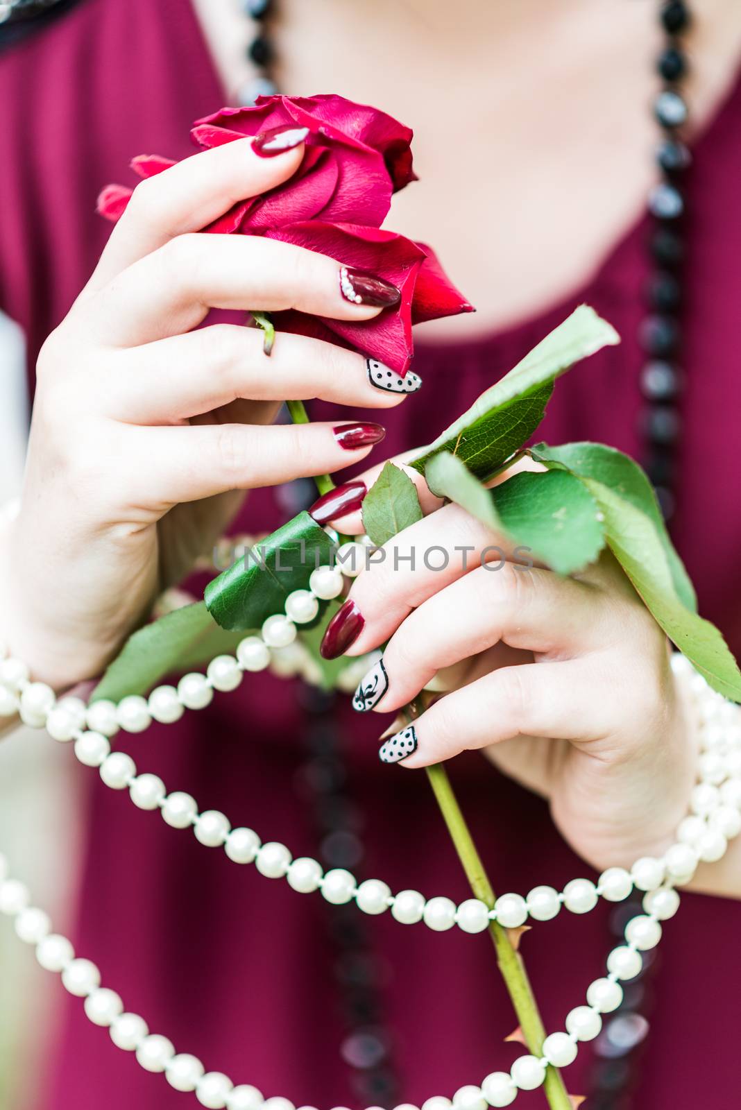 beautiful hand of a young woman with brown manicure holding red rose white pearl necklace