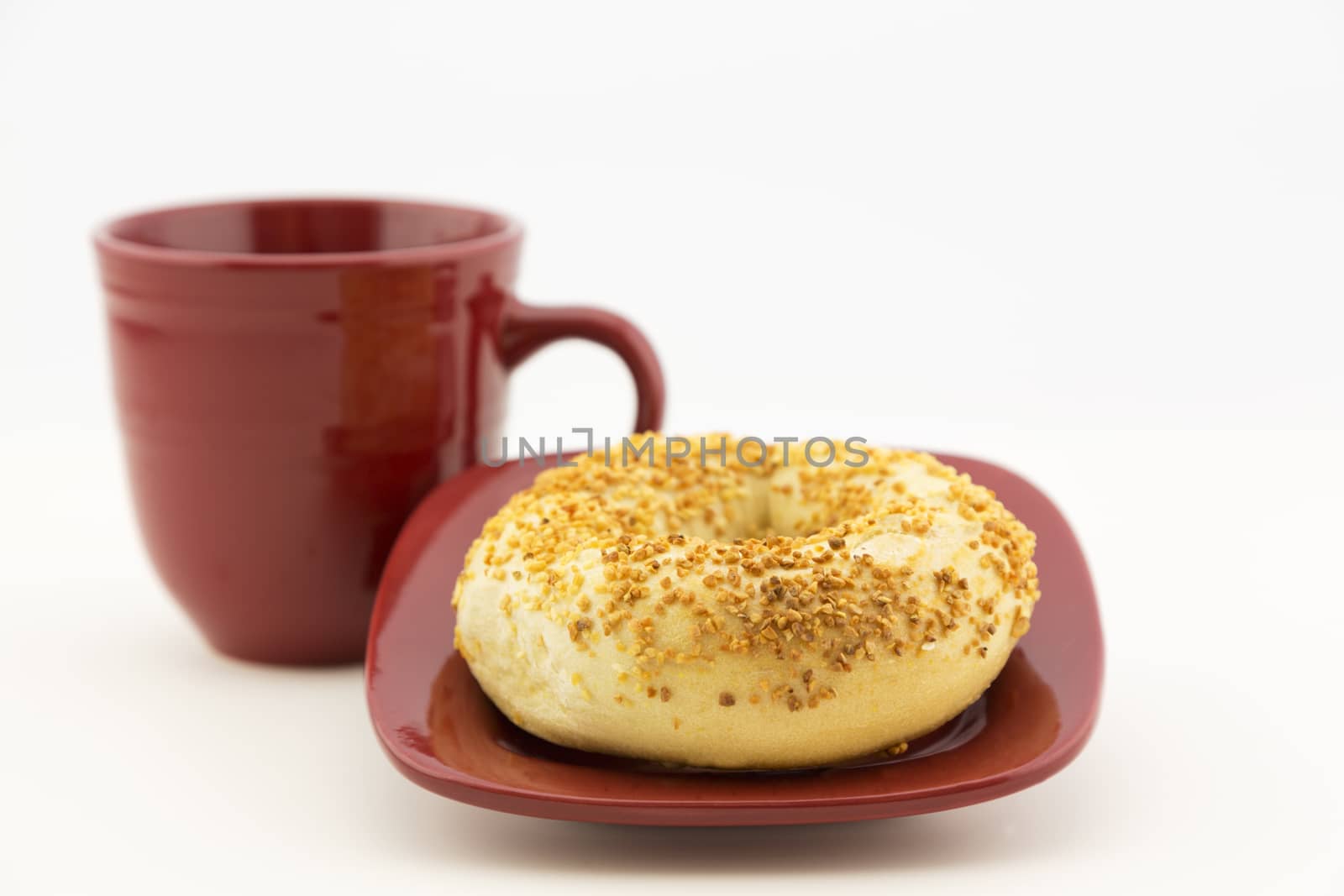 Fresh garlic bagel on square red plate with matching mug.  Horizontal food image with copy space. 