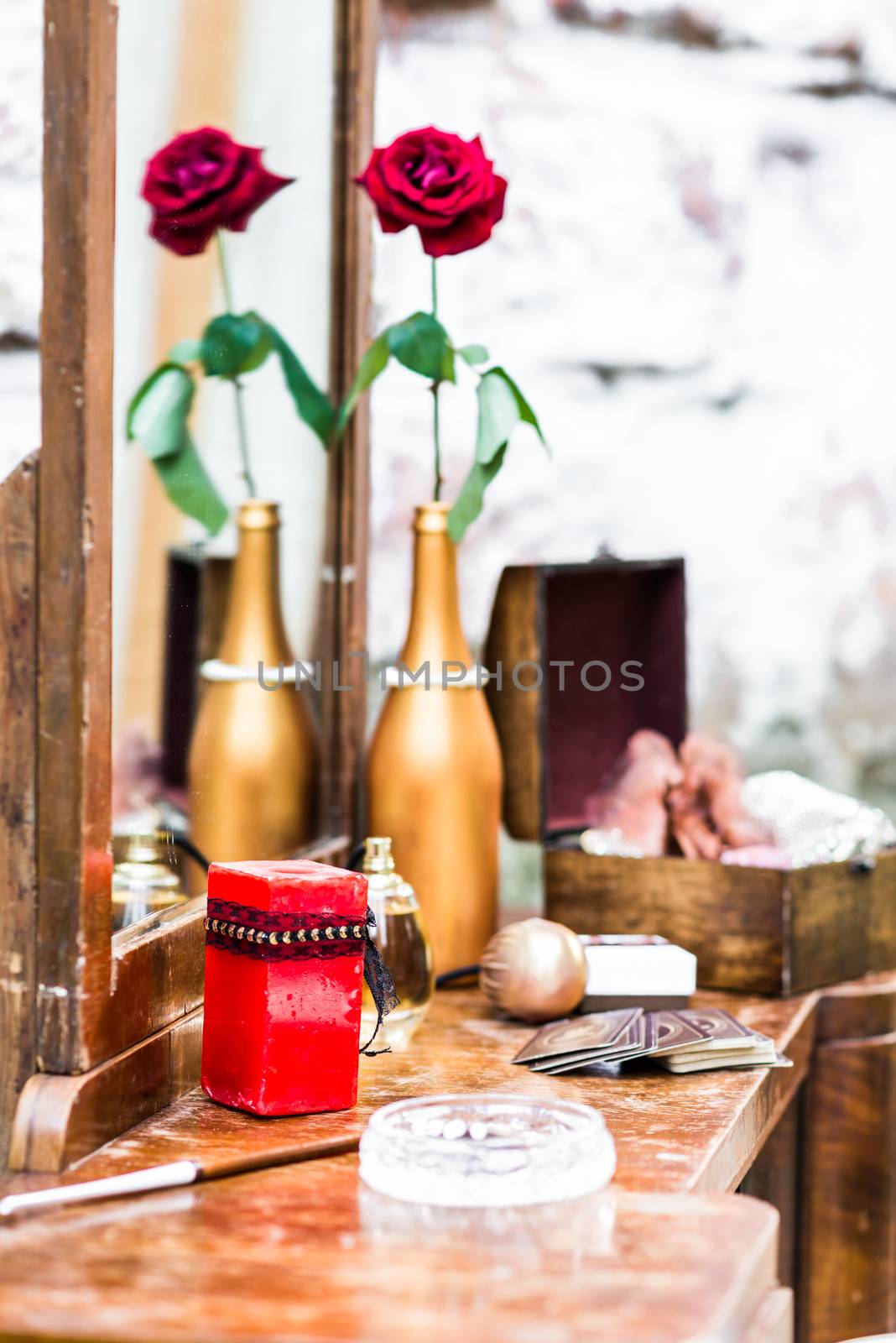 red candle on a mirror on a background of red roses in a gilded bottle