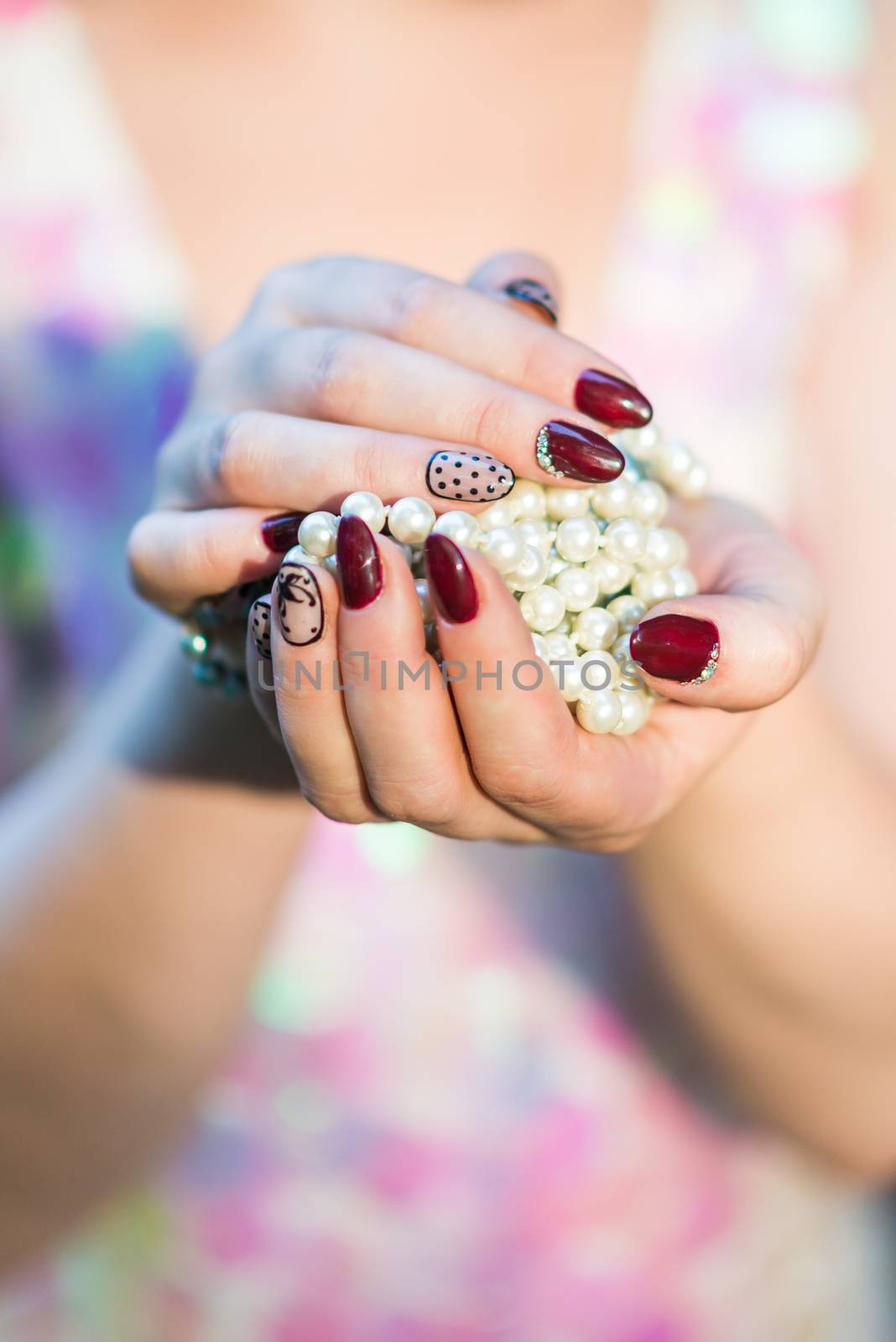 beautiful hand of a young woman with brown manicure holding white pearl necklace