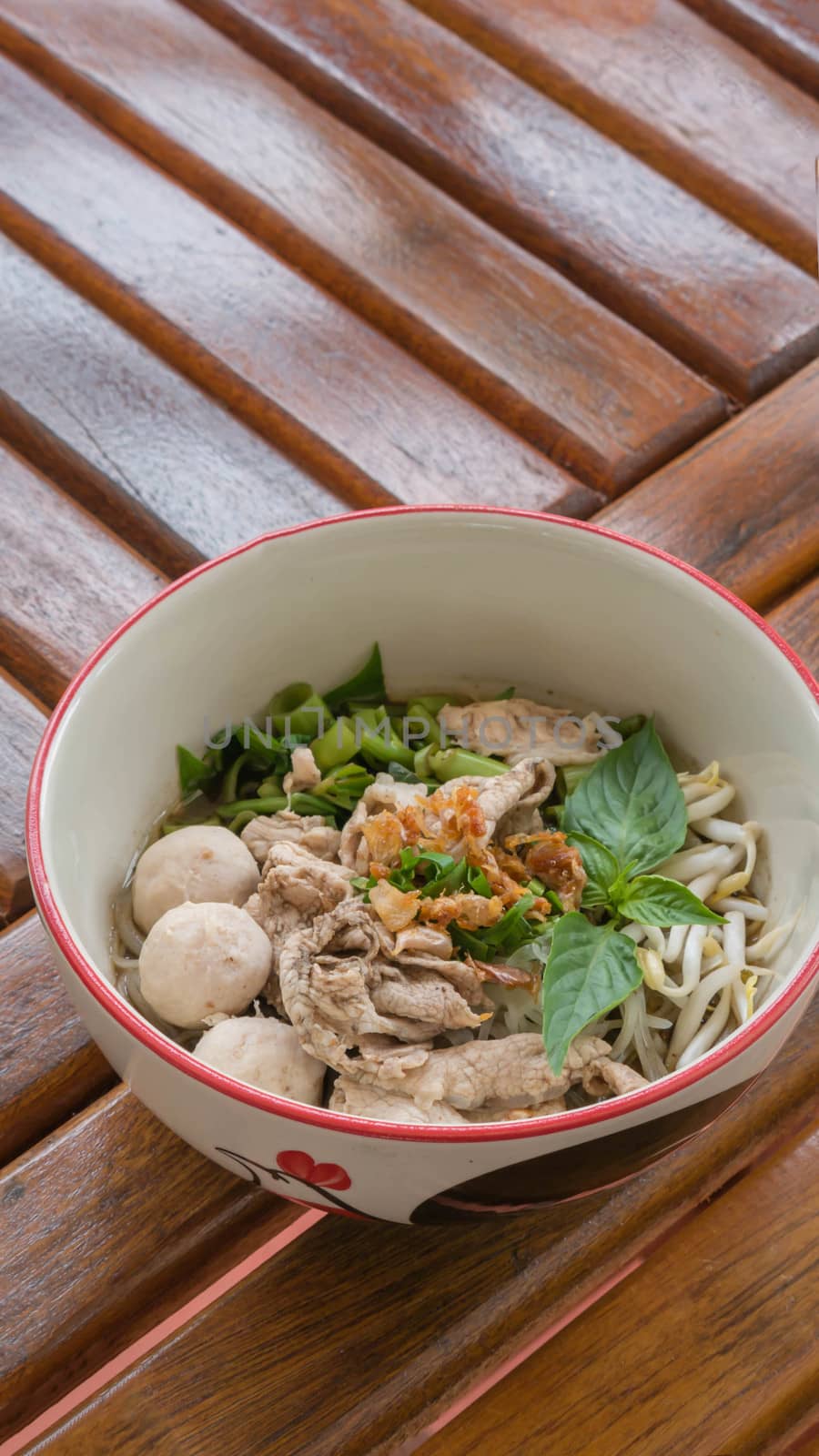 Asian white noodles with pork and vegetables in bowl over wooden background