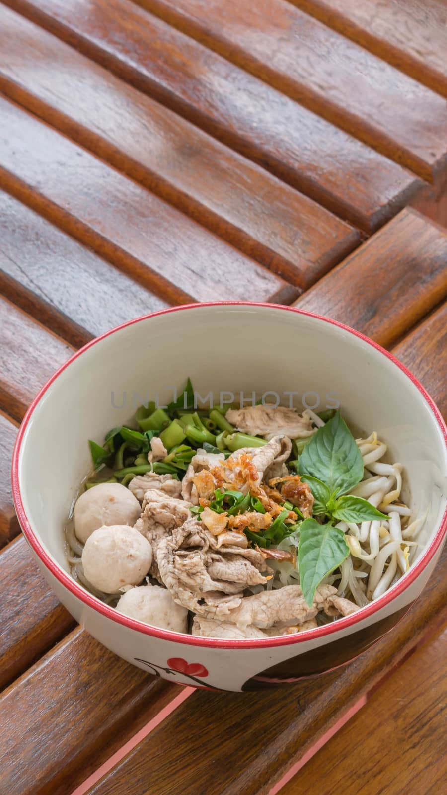Asian white noodles with pork and vegetables in bowl over wooden background