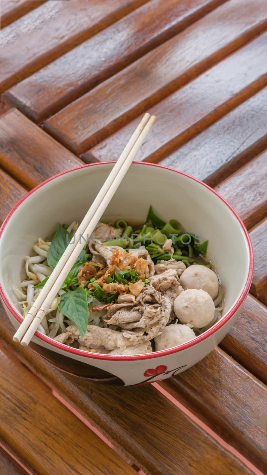 Asian white noodles with pork and vegetables in bowl over wooden background