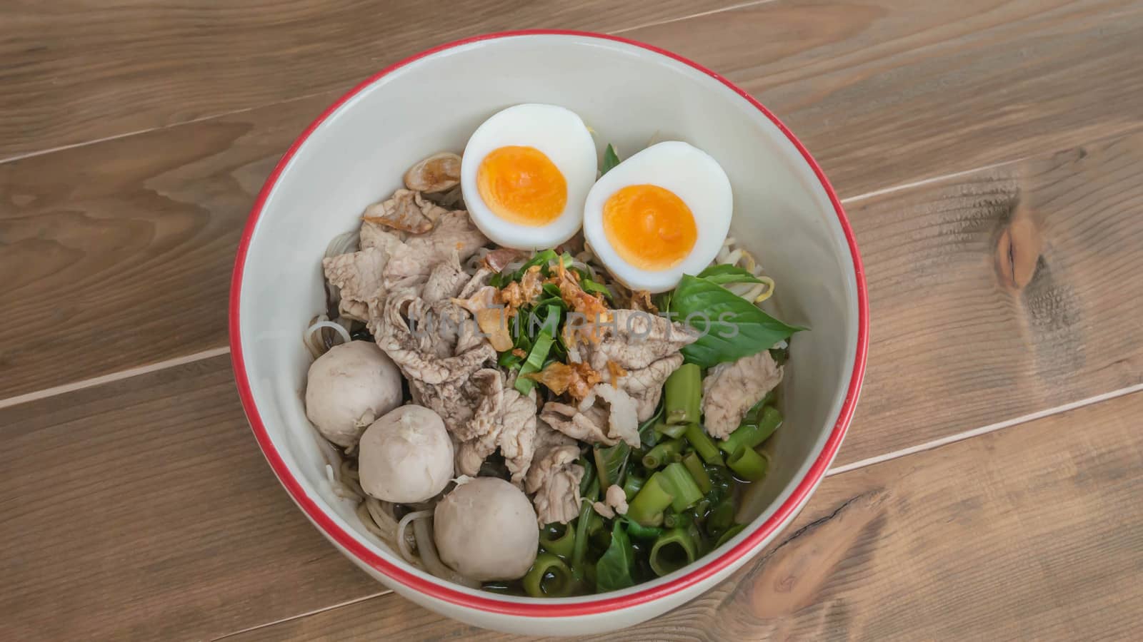 Asian white noodles with pork and vegetables in bowl over wooden background