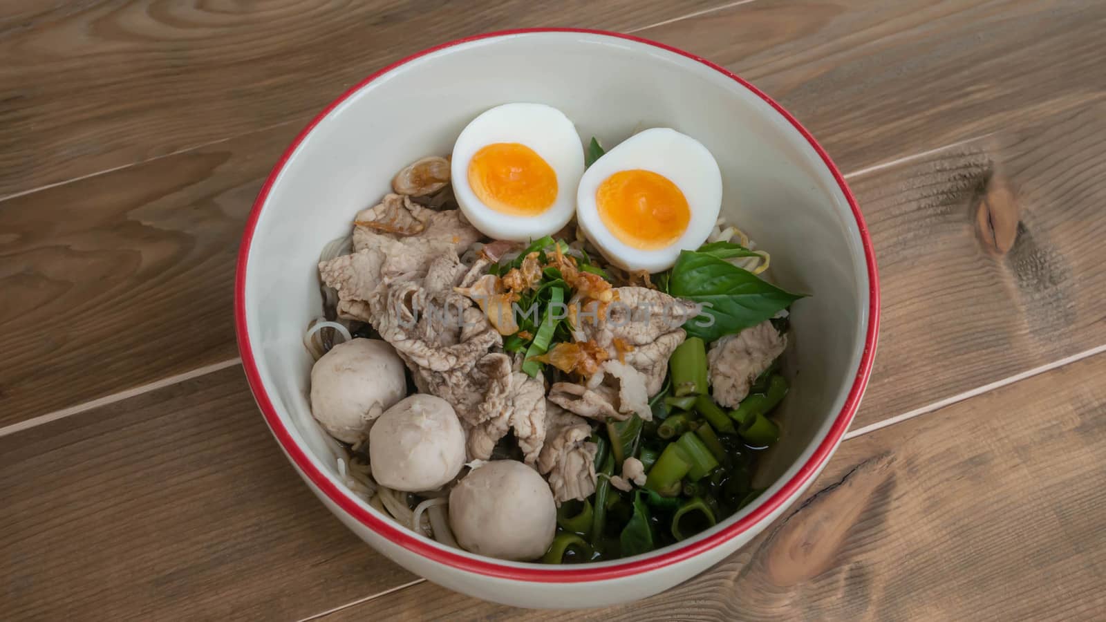 Asian white noodles with pork and vegetables in bowl over wooden background