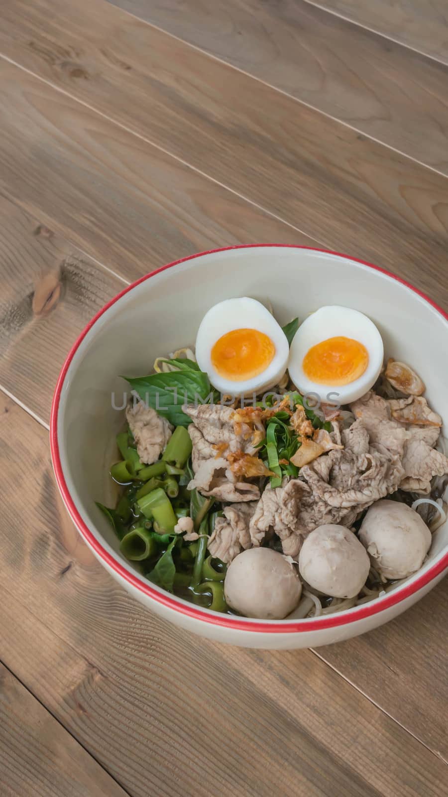 Asian white noodles with pork and vegetables in bowl over wooden background
