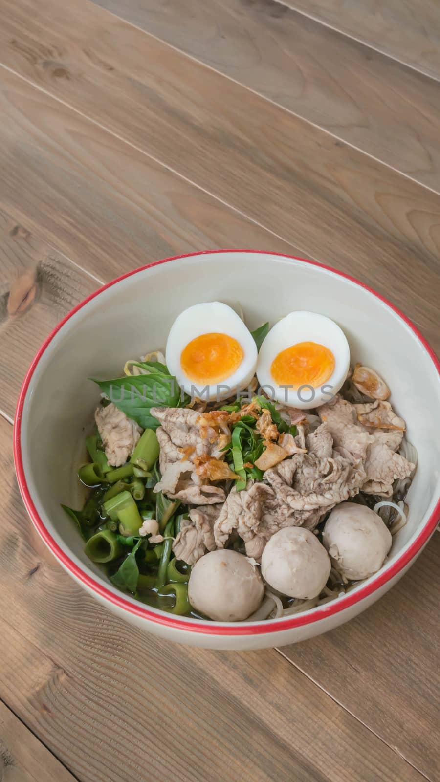 Asian white noodles with pork and vegetables in bowl over wooden background