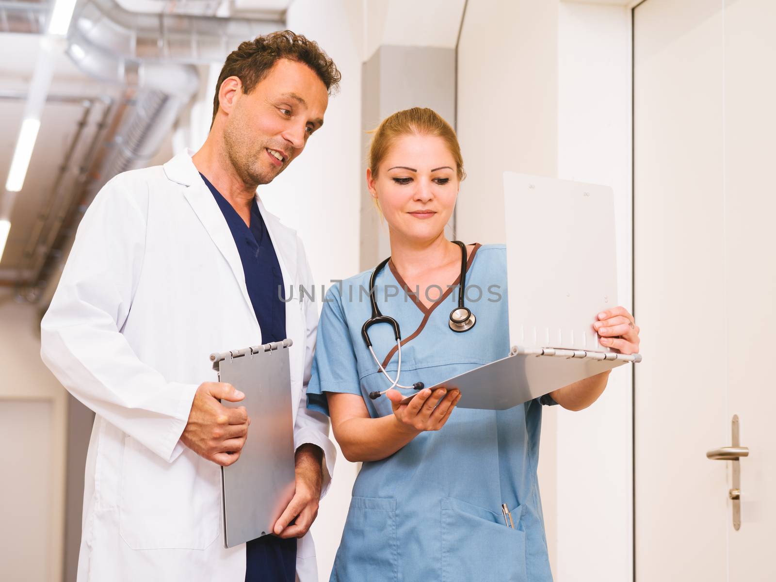Photo of a nurse and doctor discussing medical charts in the hallway of a hospital.