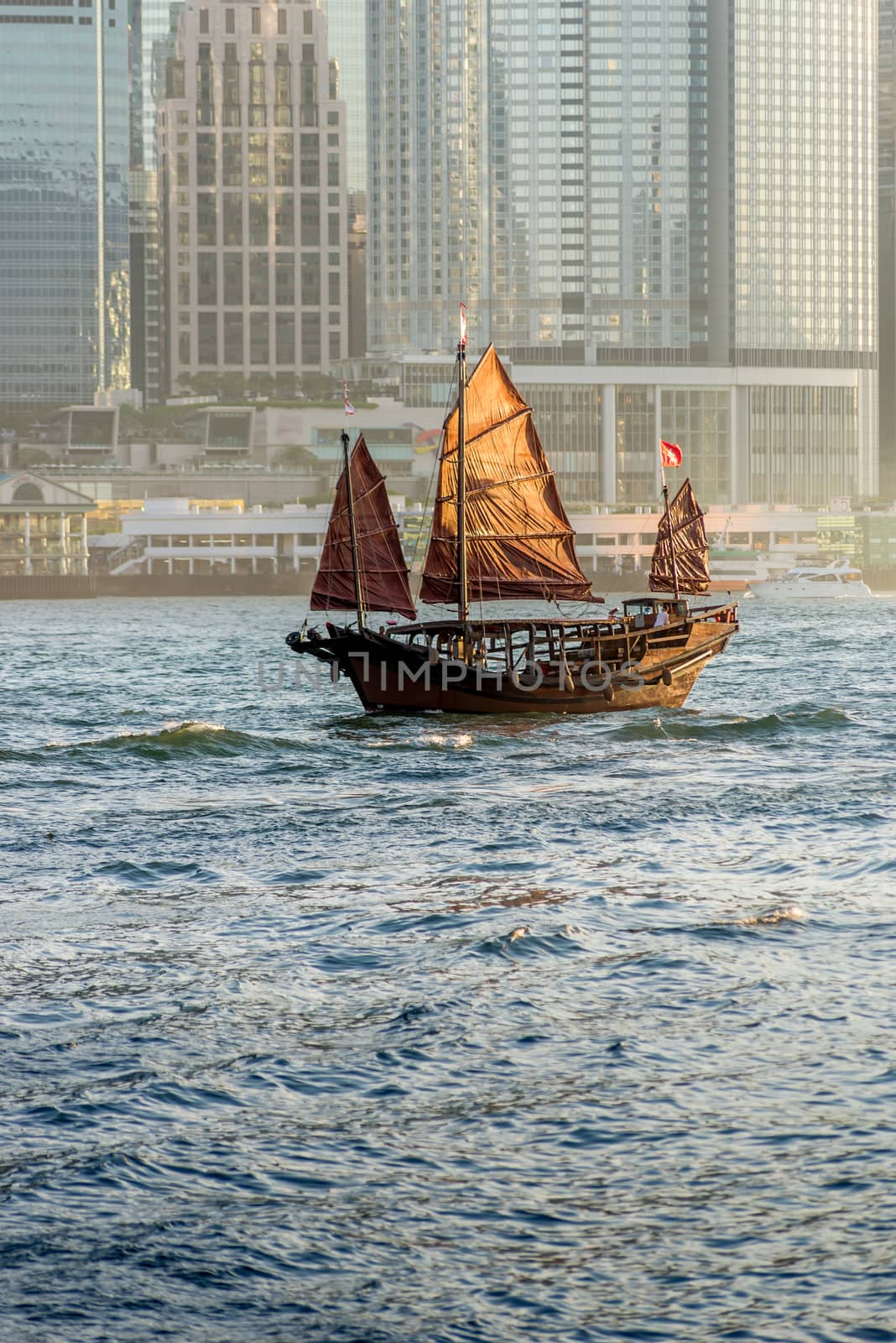 Old Junk on Hong Kong harbour with the sunlight hitting the sails and modern buildings in the background.
