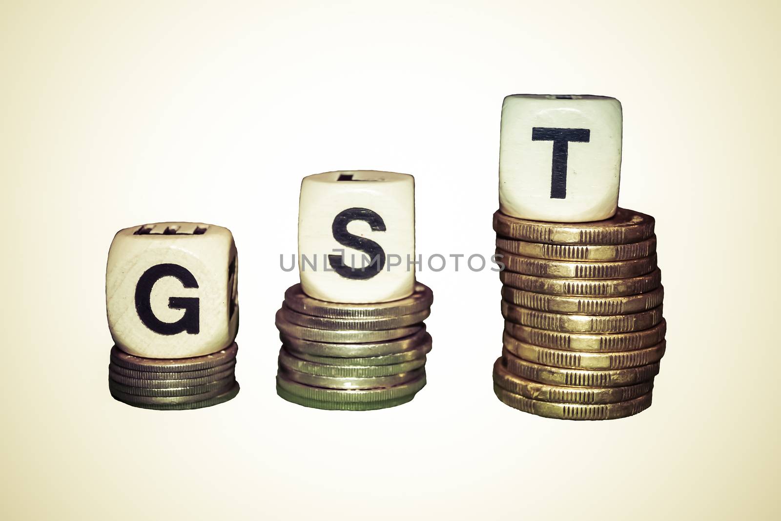 The letters G S T rising higher on on silver and gold coins.  The G is on 10 cent coins, the S on 20 cent coins and the T on one dollar coins.  The coins are against a white background.