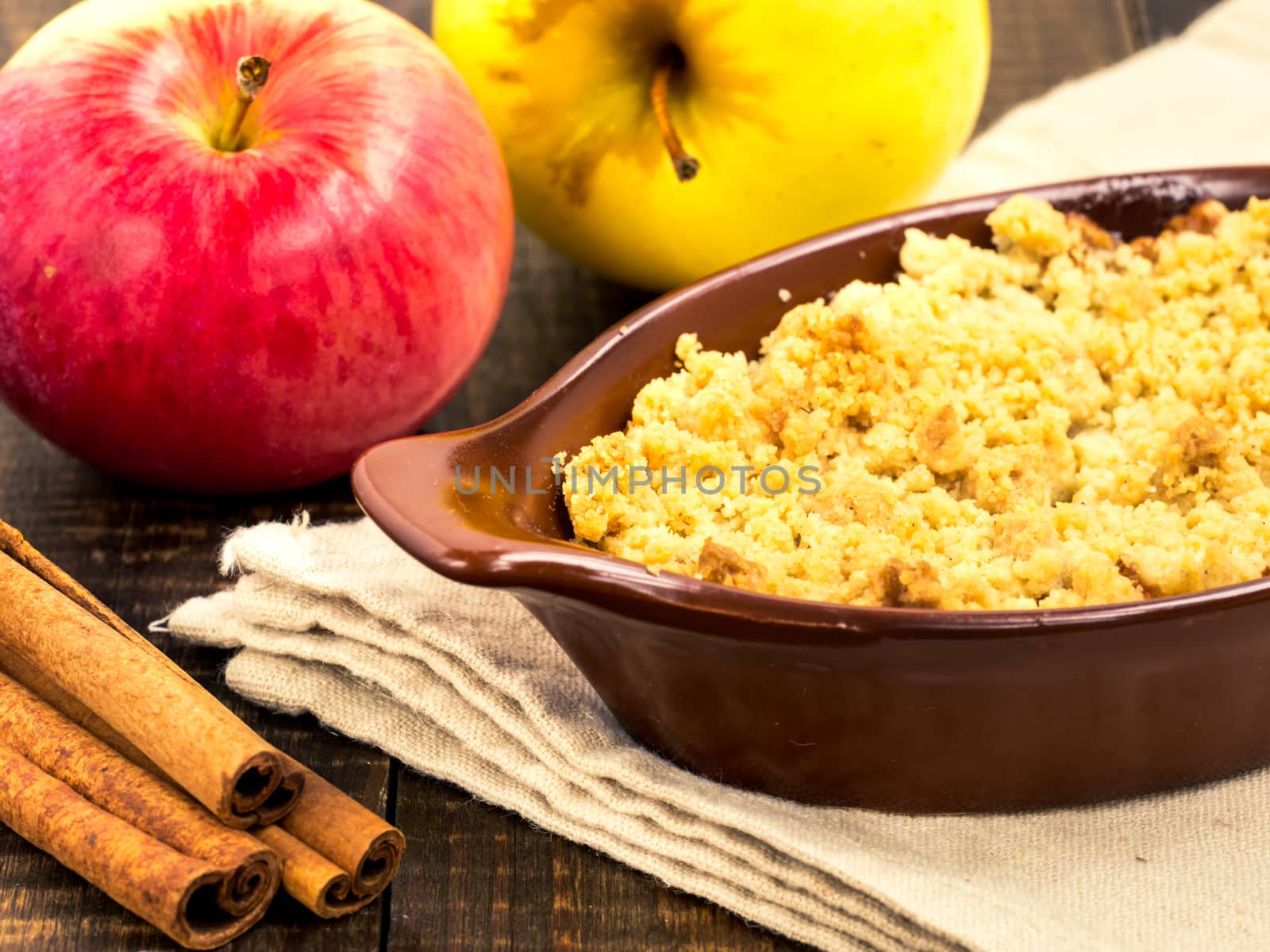 Homemade apple cramble cake with fresh apples and cinnamon sticks on rustic dark wooden background