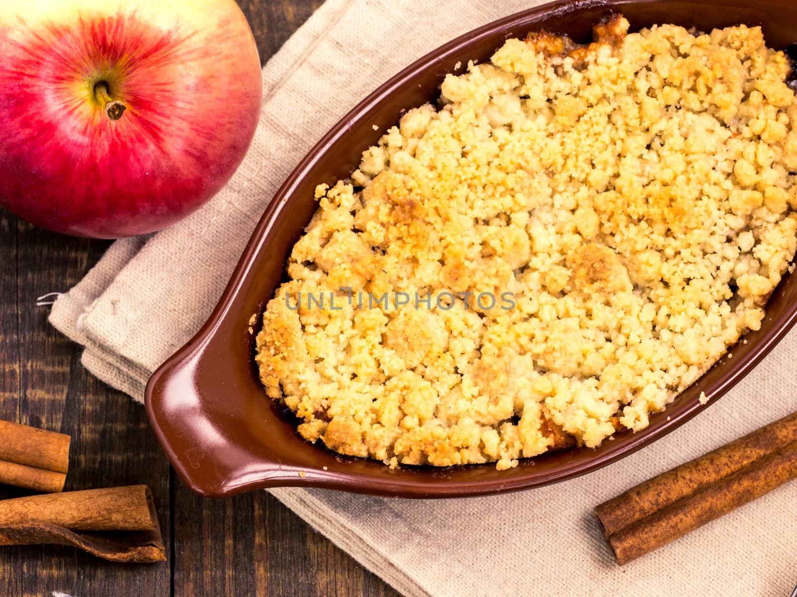 Homemade apple cramble cake with fresh apples and cinnamon sticks on rustic dark wooden background. Top view or flat lay