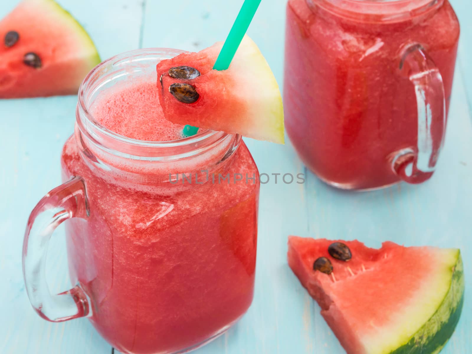 Watermelon smothie and slices on soft blue wooden background