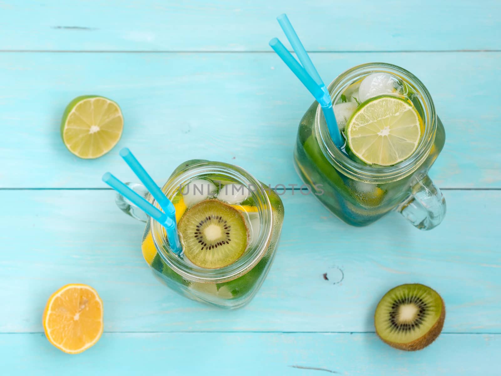 Cold homemade lemonade with fresh lemon, lime, kiwi and mint in mason jar. Summer drink on soft blue wooden background. Flat lay or top view