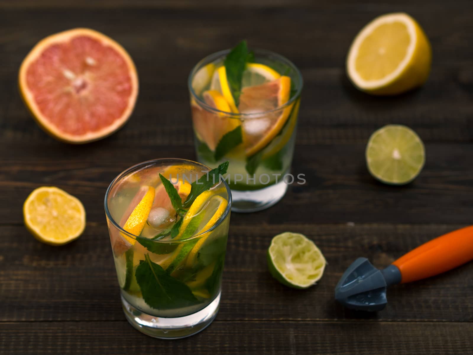 Cold homemade lemonade with fresh lemon, lime, grapefruit and mint by lemon reamer. Summer drink on dark wooden background