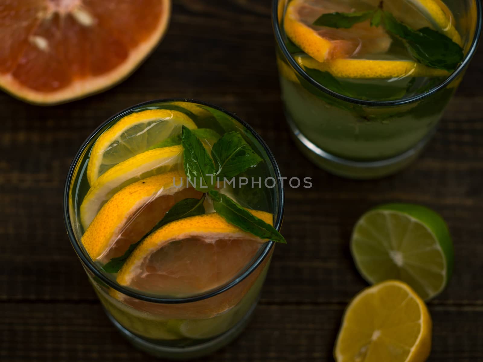 Closeup cold homemade lemonade with fresh lemon, lime, grapefruit and mint. Summer drink on dark wooden background