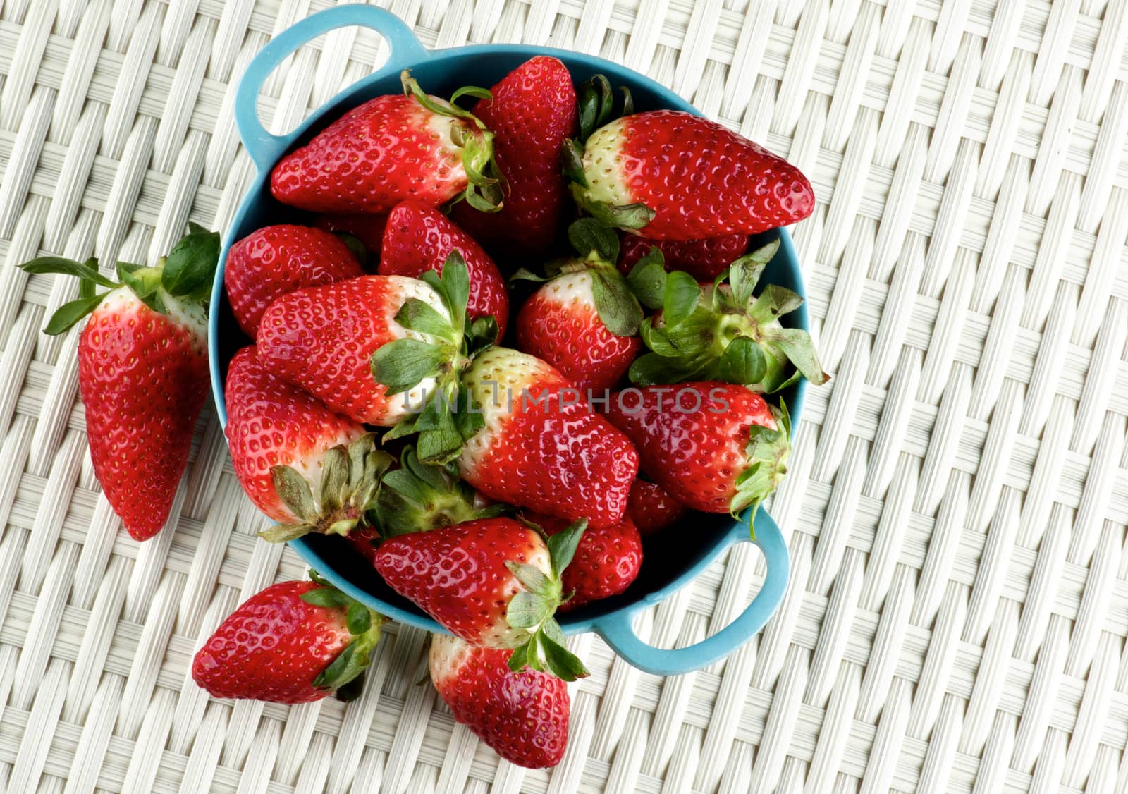 Perfect Big Ripe Strawberries in Blue Bowl closeup on Wicker background. Top View