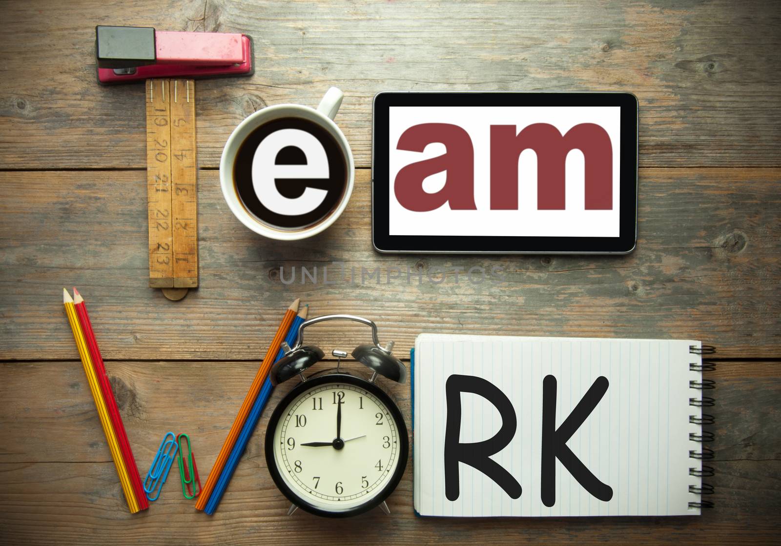 Team work spelt using stationery office tools including digital tablet, clock and notepad 