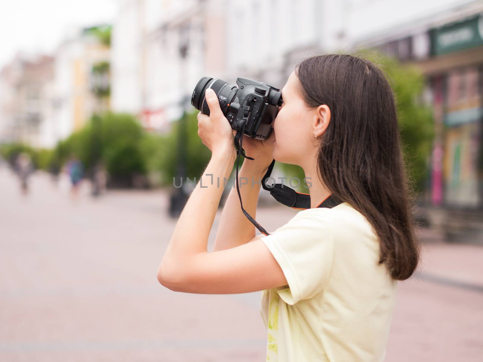 Cheerful young casual woman tourist make shots on dslr camera outdoors on city street. Vacation photography travel concept