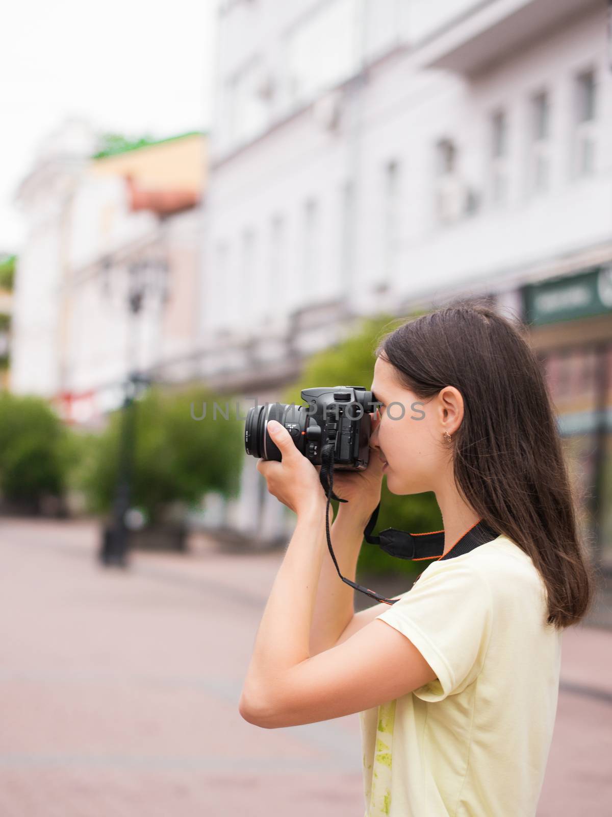 Cheerful young casual woman tourist make shots on dslr camera outdoors on city street. Vacation photography travel concept