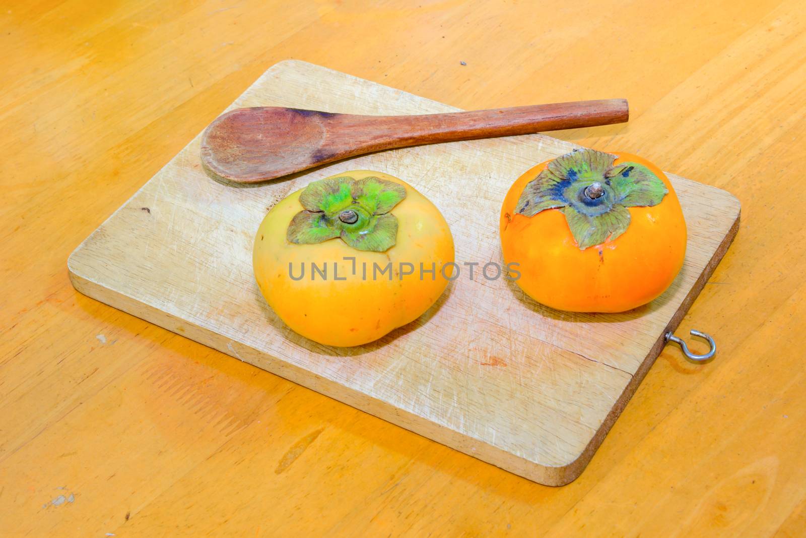 Two persimmon and Wood Spoon on the chopping block