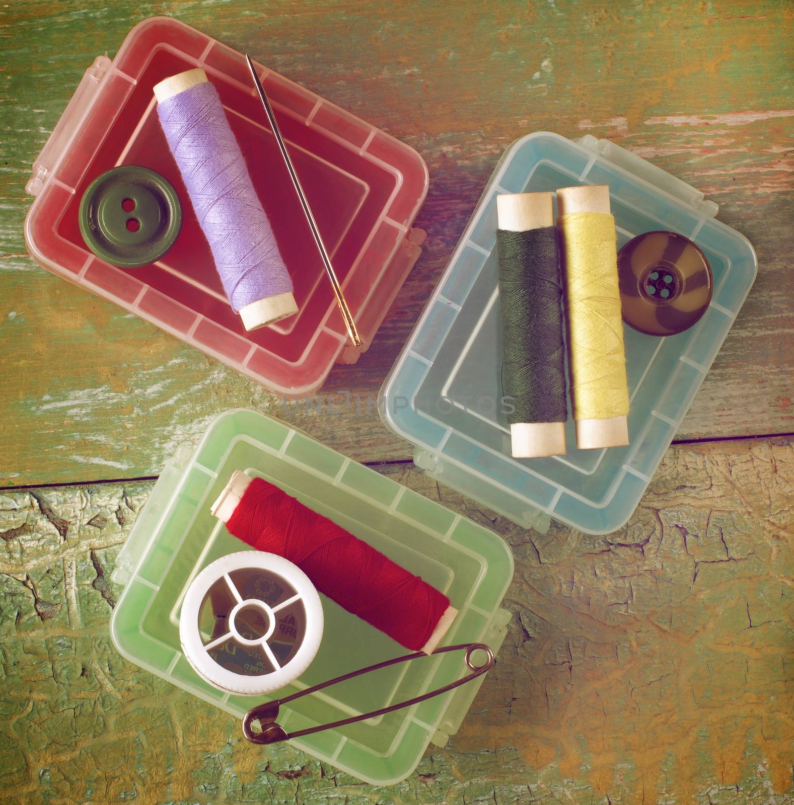 Arrangement of Plastic Sewing Boxes, Pins, Needles and Thread Spools closeup on Cracked Wooden background. Retro Styled