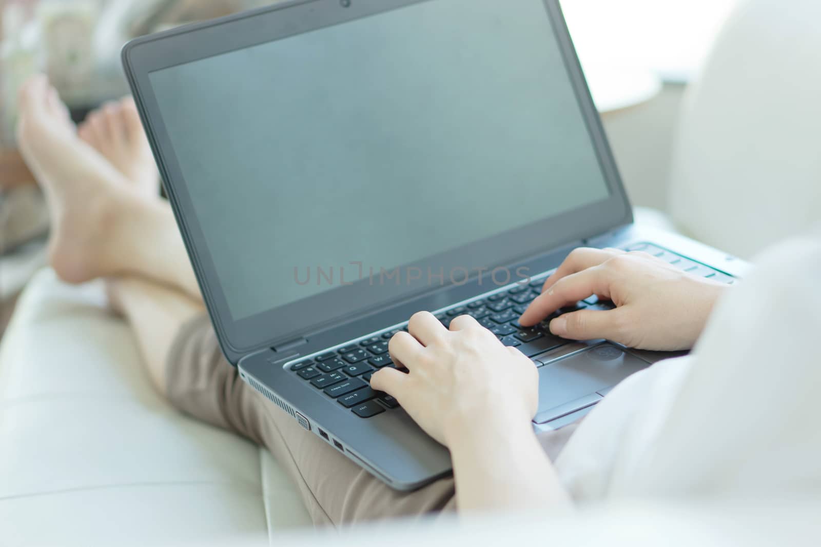 Side view of casual young woman using laptop on sofa at home