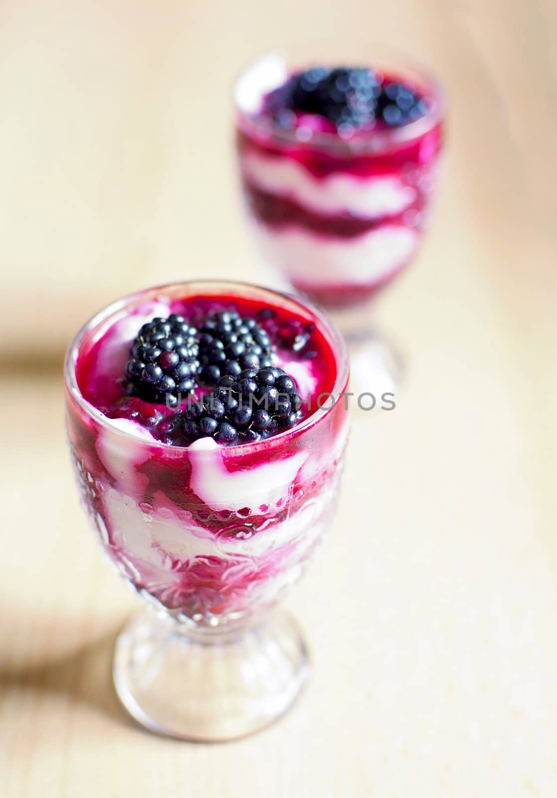 Glass cups with cream cheese blackberry desserts. Fresh blackberries are placed on top of the desserts.