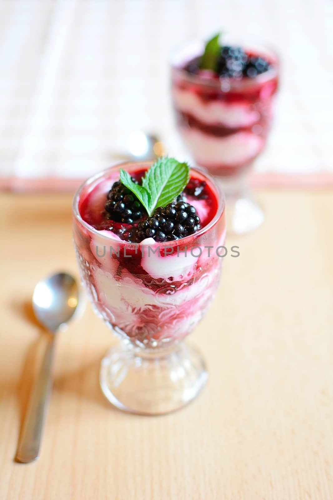 Glass cups with cream cheese blackberry desserts. Fresh blackberries and mint leaves are placed on top of the desserts.