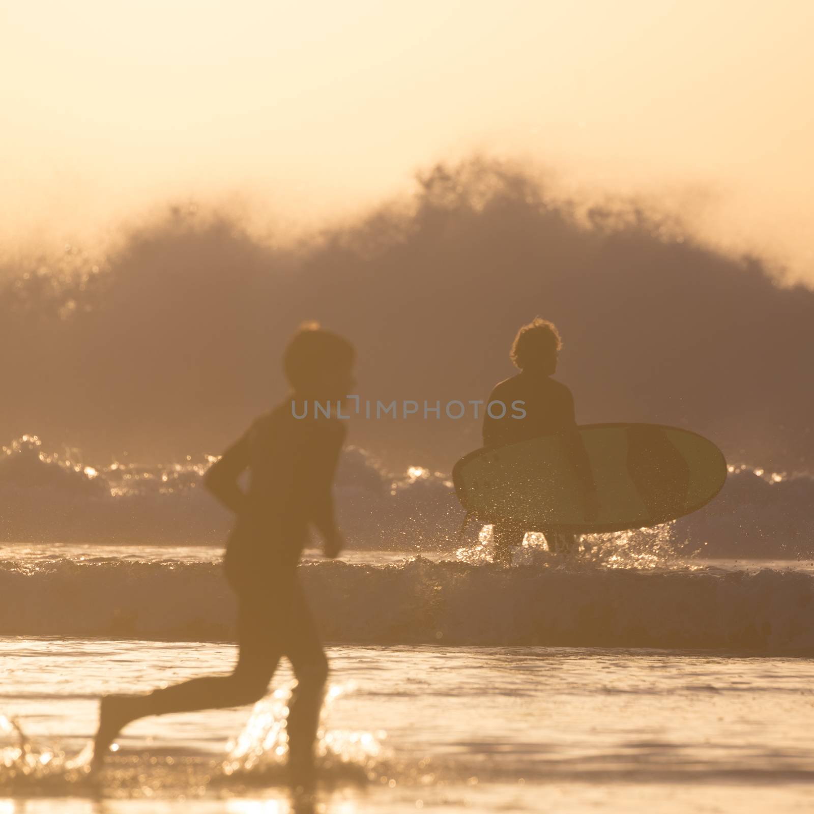 Silhouette of surfers on beach in sunset. by kasto