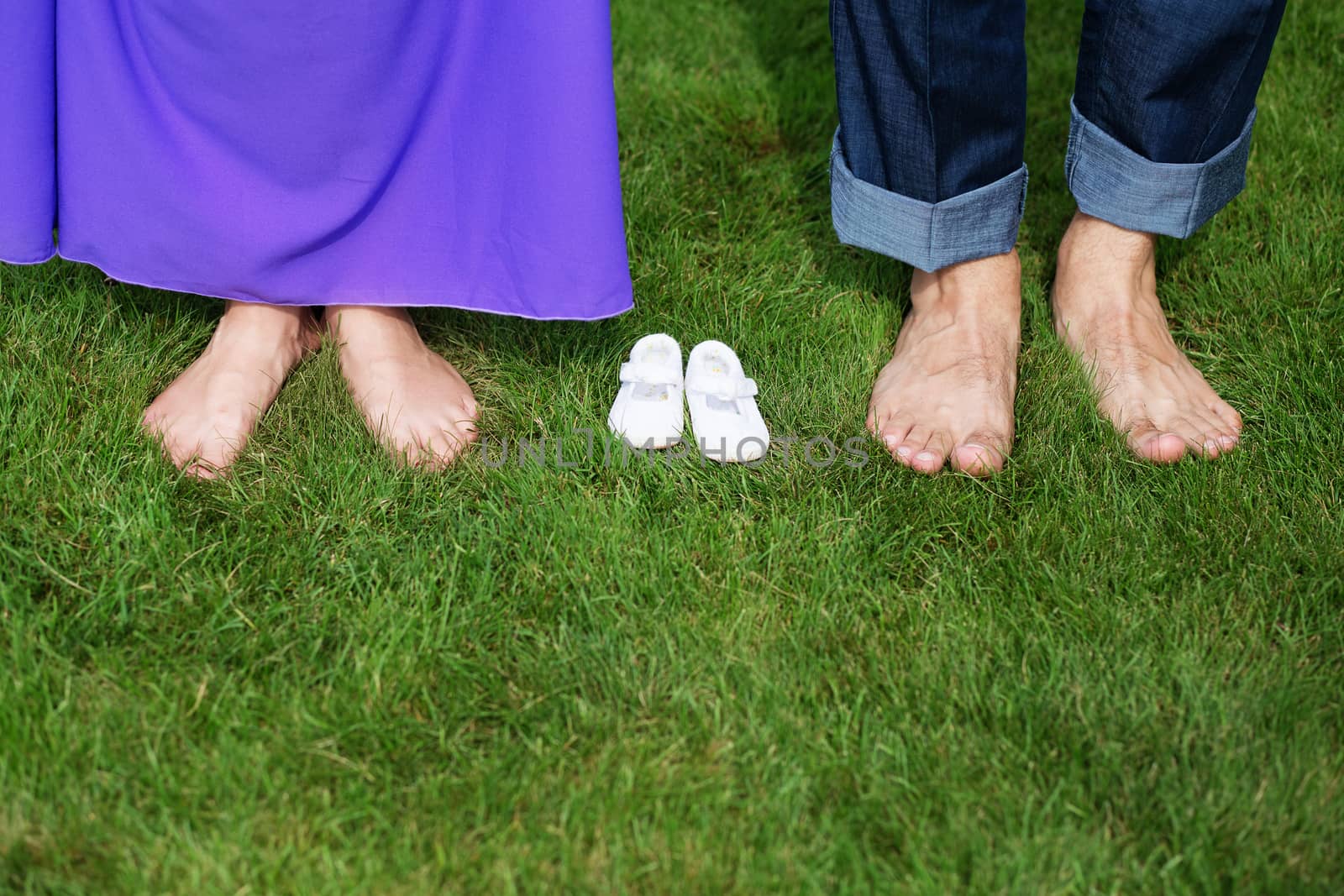 Young Pregnant Couple Feet barefoot on green grass With Newborn Baby Booties In Nature
