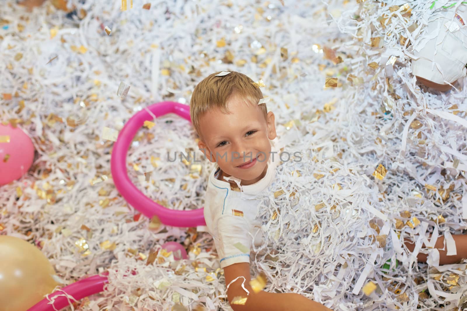 Little boy jumping and having fun celebrating birthday. Portrait of a child throws up multi-colored tinsel and paper confetti. Kids party. Happy excited laughing kid under sparkling confetti shower