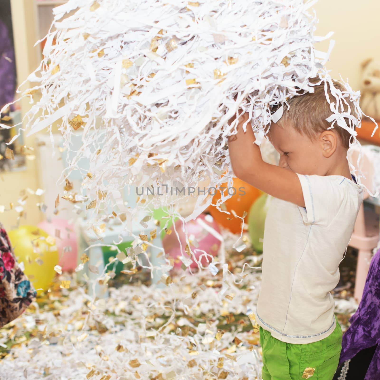 Little boy jumping and having fun celebrating birthday. Portrait of a child throws up multi-colored tinsel and paper confetti. Kids party. Happy excited laughing kid under sparkling confetti shower