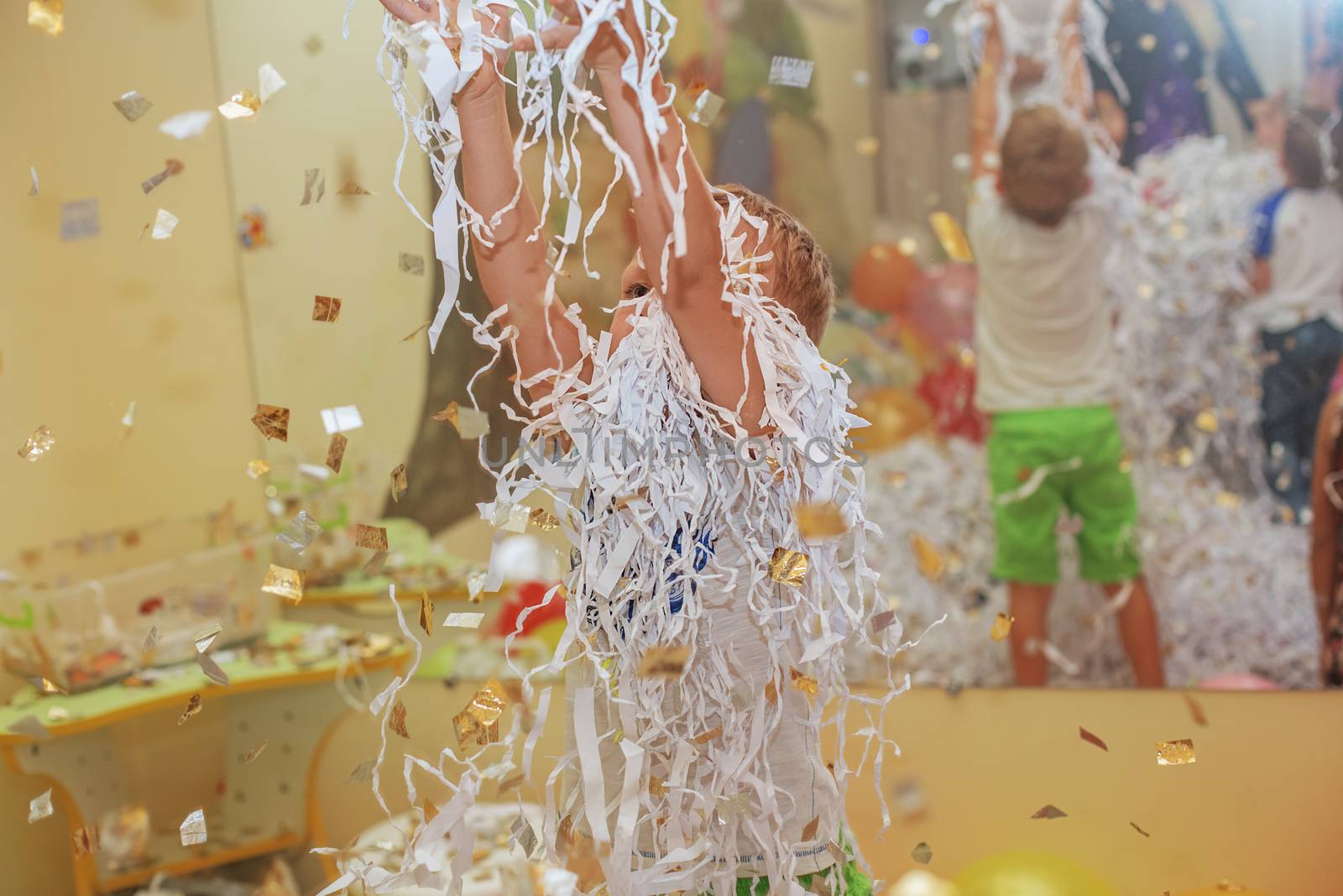 Little boy jumping and having fun celebrating birthday. Portrait of a child throws up multi-colored tinsel and paper confetti. Kids party. Happy excited laughing kid under sparkling confetti shower