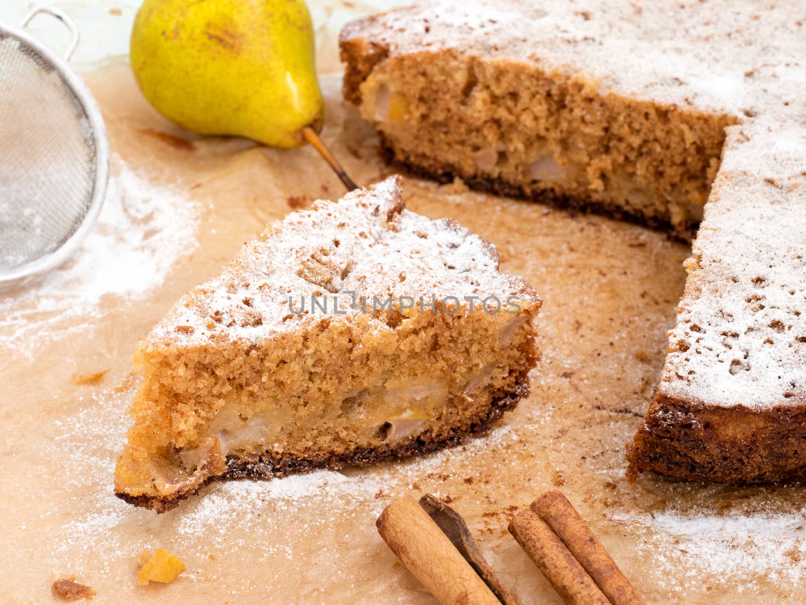Homemade pears cake with fresh pears and cinnamon sticks with powdered sugar on baking paper background