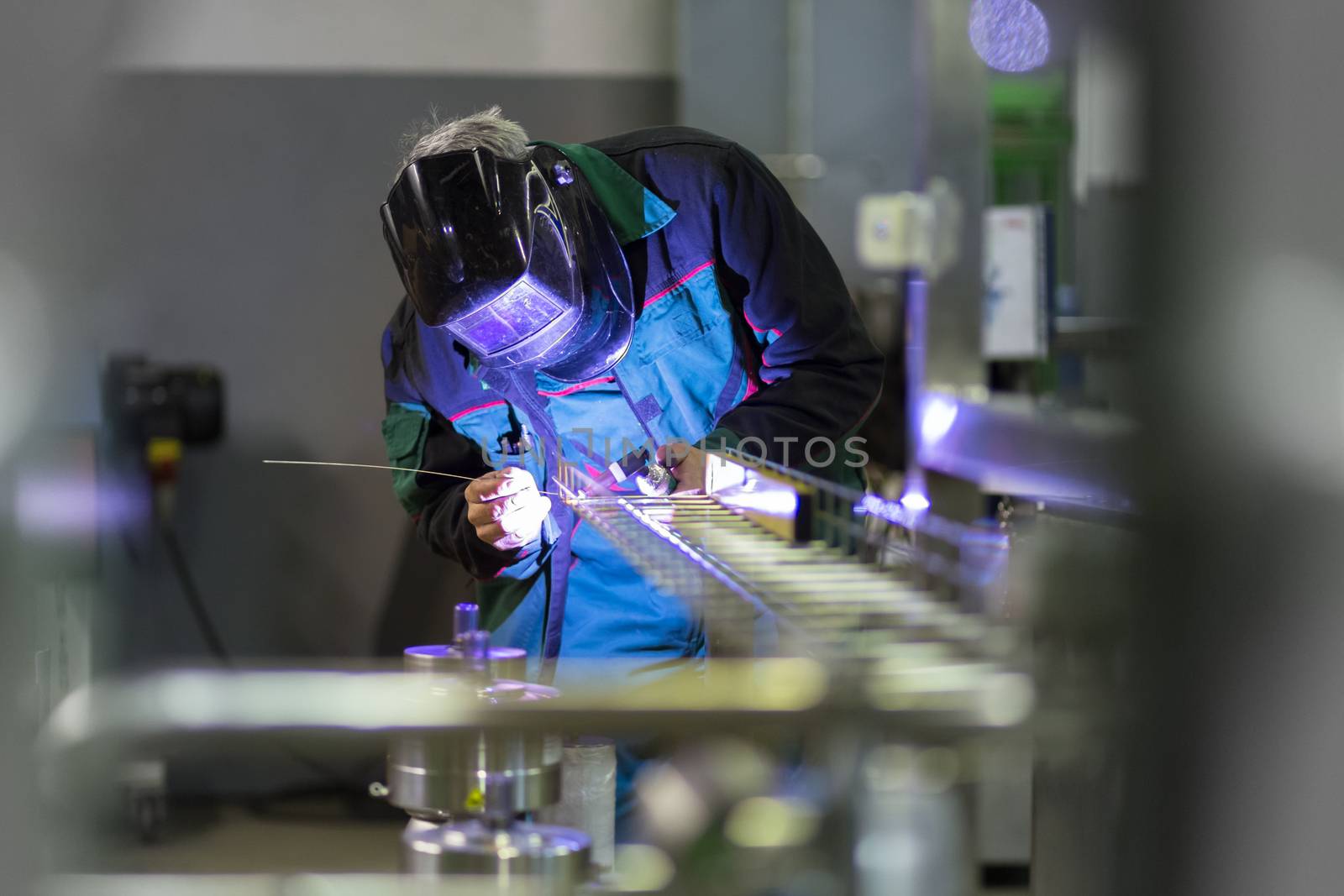 Industrial worker with protective mask welding inox elements in steel structures manufacture workshop.