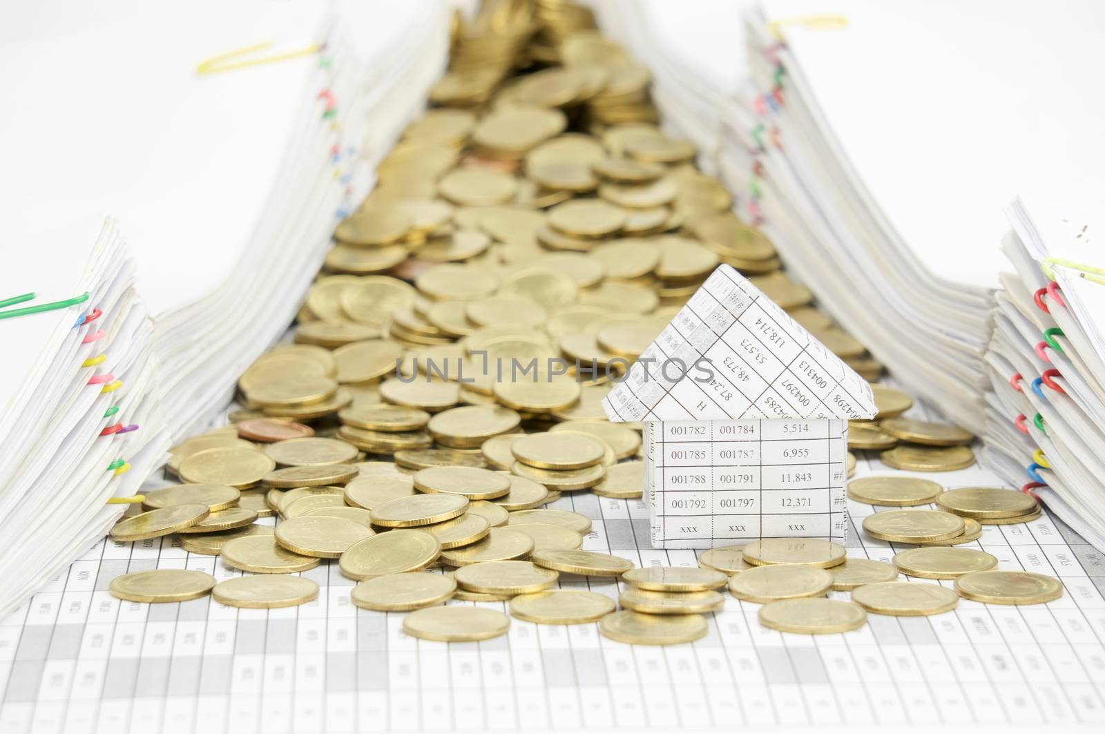 House with stack of gold coins on finance account have pile of document with colorful paperclip as background.