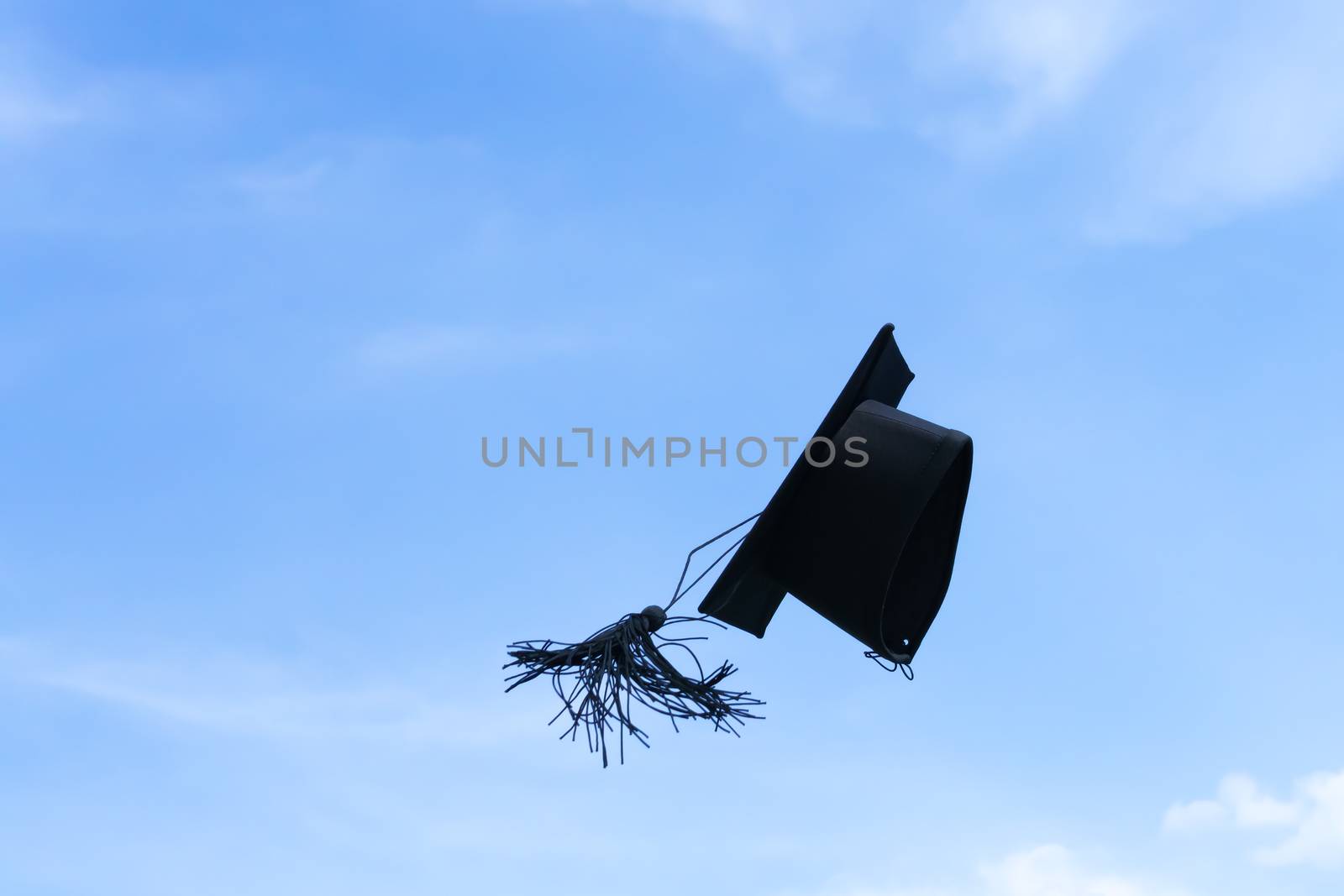 One graduation cap or mortar board thrown up to the air, sky background by beer5020