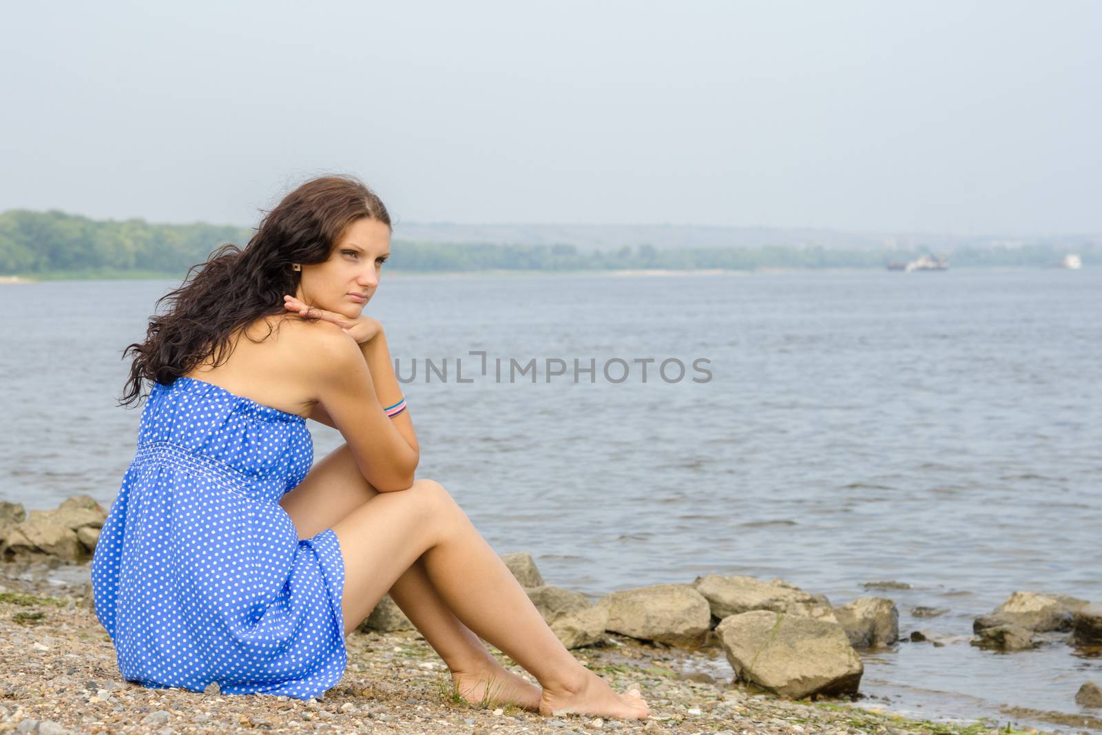 Lonely sad young girl sitting on the river bank