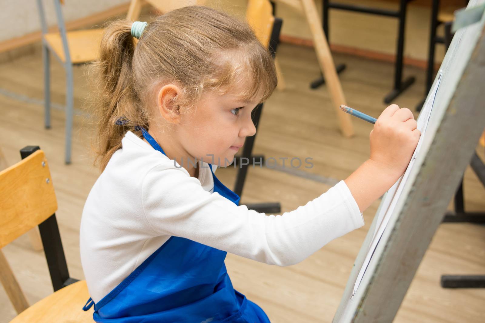Five-year girl paints on an easel in the drawing lesson