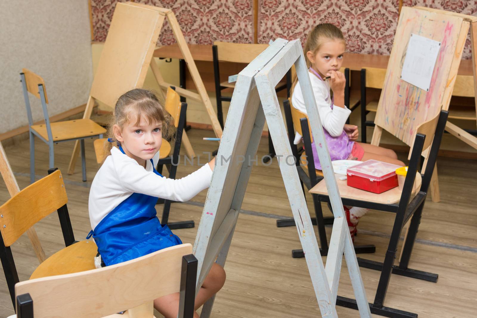 Two girls at a drawing lesson listen to the teacher's explanations